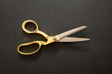 Pair of scissors gold handle on black background, top view