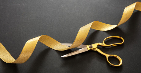 Grand opening. Gold scissors cutting gold satin ribbon, black background