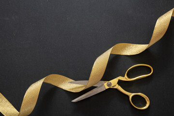Grand opening. Gold scissors cutting gold satin ribbon, black background