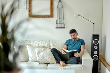 Hombre leyendo un libro en casa. Concepto confinamiento. - obrazy, fototapety, plakaty