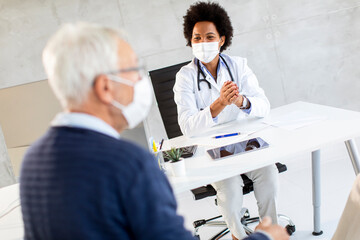 Naklejka premium Senior couple with protective facial masks receive news from black female doctor