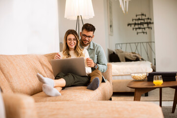 Young couple using laptop together while sitting on sofa at home