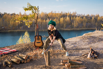 The group of young people are resting in nature. girl chopping wood for a fire with an ax.
