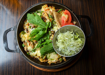 Appetizing pan with fried potatoes with meat and cheese, supplemented with greens, salad and tomato