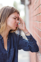 Very sad looking woman holds her head against a brick wall. Selective focus.