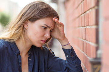 Very sad looking woman holds her head against a brick wall. Selective focus.