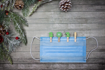 Medical mask with clothespins in the form of the numbers 2021 on a wooden background and New Year's branches. Copy space for text