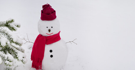 Snowman wearing a winter hat. scarf on white background and standing by a tree.