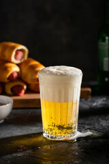 A glass of light beer with foam and sausages in the dough on the wooden board