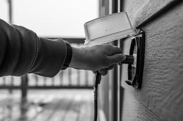 Hand gripping power cord and lifting cover of an outdoor GCFI outlet to plugin
