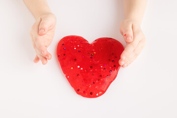 Red slime in heart shape in kid hands. Kid hands playing slime toy on white background. Making slime. Love and valentines day concept