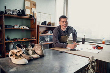 An experienced shoemaker in a shoe production workshop makes a pattern for a shoe from paper with...