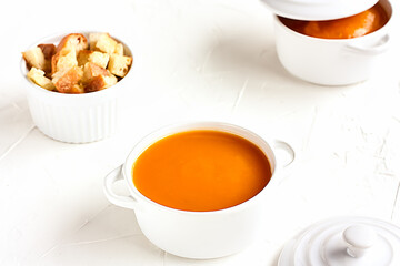 Vegetarian spicy autumn pumpkin cream soup served in white cocotte with croutons and pumpkin seeds on white background.Seasonal autumn vegetarian food