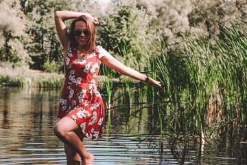 young brunette girl in a red dress on a background of the river with reeds