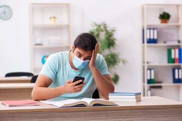 Young male student sitting in the classroom wearing mask