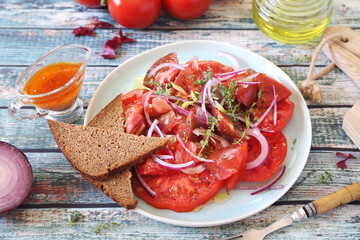 Tomato salad with red onion and spicy sauce of different varieties of tomatoes, two slices of rye bread