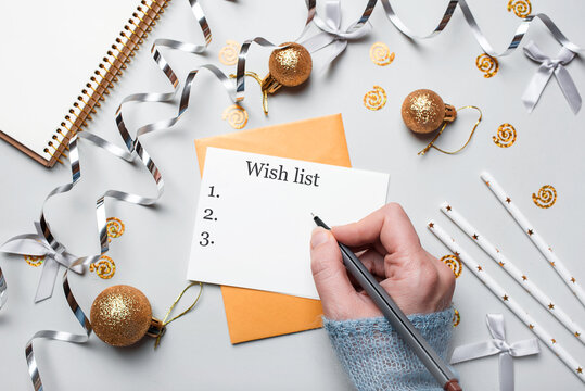 Happy New Year 2021. Woman's hand writing in notebook decorated with Christmas decorations on the grey background. Top view, flat lay