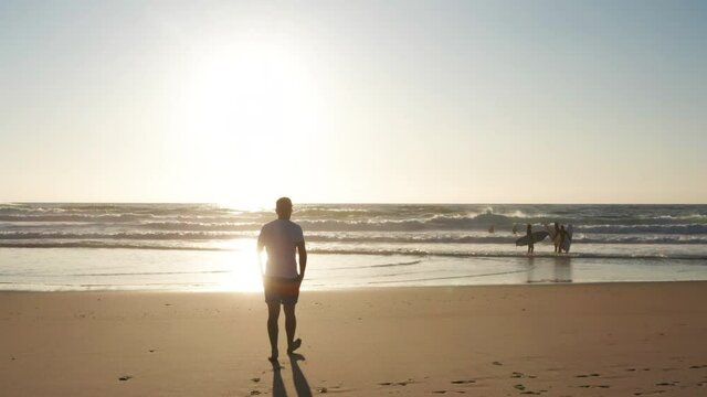 Man is walking in front of the sun, sandy beach, Surfers in backlighting at the ocean leaving the beach, view of people silhouette at the beach near Hossegor in France during a sunset
