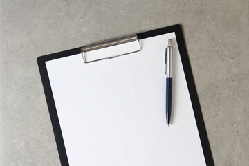 Template of white paper with a ballpoint pen on light grey concrete background in a black tablet with a clip. Concept of new idea, business plan and strategy,  empty space for text