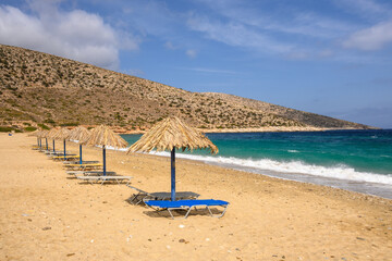 Sun beds and umbrellas at Agia Theodoti beach on Ios Island. A wonderful beach with the golden sand and azure waters. Cyclades, Greece