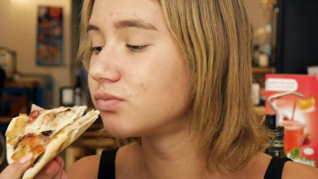Portrait of a 13 years old girl biting pizza slice in restaurant. Close-up shot.