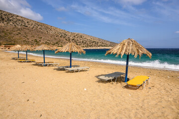 Sun beds and umbrellas at Agia Theodoti beach on Ios Island. A wonderful beach with the golden sand and azure waters. Cyclades, Greece