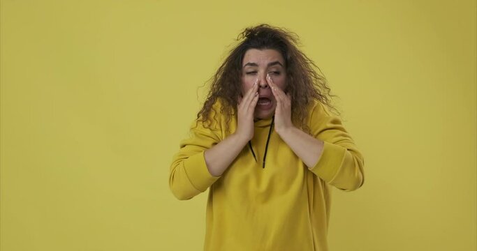Sick woman covering mouth with hands while sneezing over yellow background
