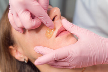 Beautician depilation young woman's face with wax in spa center close up