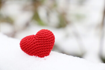 Fototapeta premium Love heart, red knitted symbol of passion in the snow in winter park. Background for Valentine's card