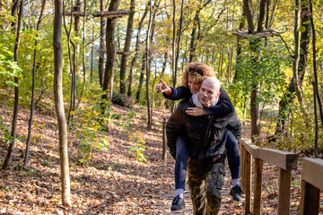 Young couple hiking through the woods. Boyfriend gives his girlfriend a piggyback ride up the forest trail. Leisure and fun concept.