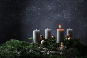 First advent with one burning candle on fir branches with Christmas decoration against a dark grey...