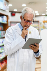 Senior pharmacist working on tablet in his store