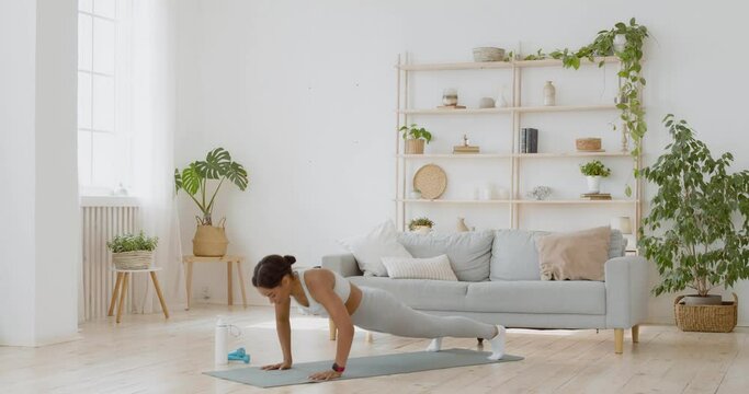 Fitness black woman practicing burpee workout at home, doing push ups and jump exercise