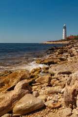 The white lighthouse stands on the seashore. In the foreground are picturesque stones