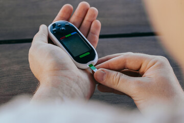 medicine, diabetes, glycemia, healthcare and people concept - man checking blood sugar with glucometer and test strip at home.