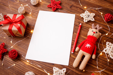 Christmas composition greeting card. Gift with amigurumi deer with decoration and paper blank for goals, plan or wishlist to santa. Mockup. Top view, flat lay, copy space.