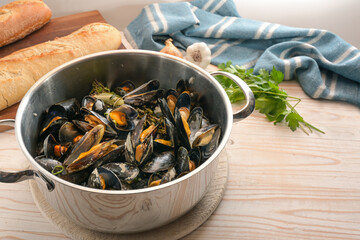 Freshly cooked mussels in a pot, bread, herbs and a blue towel on a wooden kitchen table, healthy seafood meal, copy space, selected focus, narrow depth of field