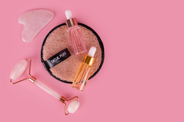 Jade face roller and Gua sha stone for facial massage. Home skin care anti-aging tools, face serum bottle, massage roller. Natural organic essential oil, skincare beauty product. Flat lay, top view.