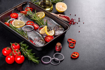 Raw trout lie on a black stone chopping board on a dark concrete table