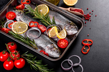 Raw trout lie on a black stone chopping board on a dark concrete table