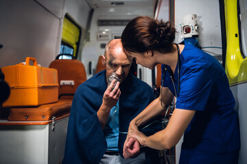 A female paramedic checking her patient's pulse and asking him questions.