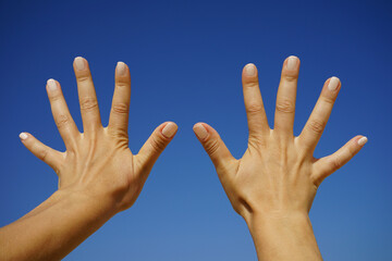 women's hands show the number ten against a cloudless blue sky