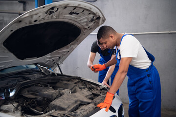 Two male mechanics in uniform inspect a car engine