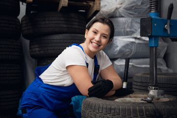 Woman in work clothes posing next to wheels and a machine tool and smiles