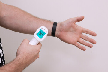 Man is measuring temperature himself using digital infrared thermometer at hand wrist