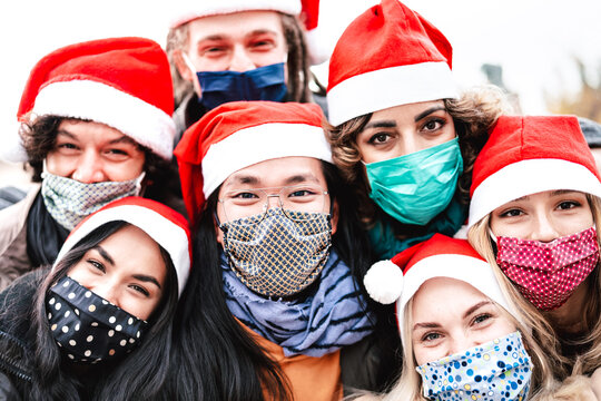Close up photo of friends taking selfie wearing face mask and santa hat - New normal Christmas holiday concept with people having fun together outdoors - Bright filter with focus on central asian guy