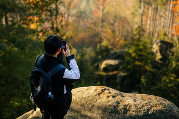 Tourist takes a photo on his smartphone, sandstone landscape of Bohemian Paradise, sunny day, rock formation Besednicke skaly (Besednicke rocks), Mala Skala, Czech Republic