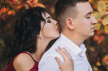 A beautiful and in love brunette girl with curly hair kisses her beloved boyfriend on the neck. Close-up portrait of lovely newlyweds.