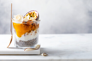 Healthy tropical fruit chia pudding with granola, mango, passion fruit and coconut chips in a glass...