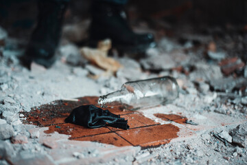 Broken molotov cocktail on the floor of abandoned building near the legs of soldier in heavy boots
